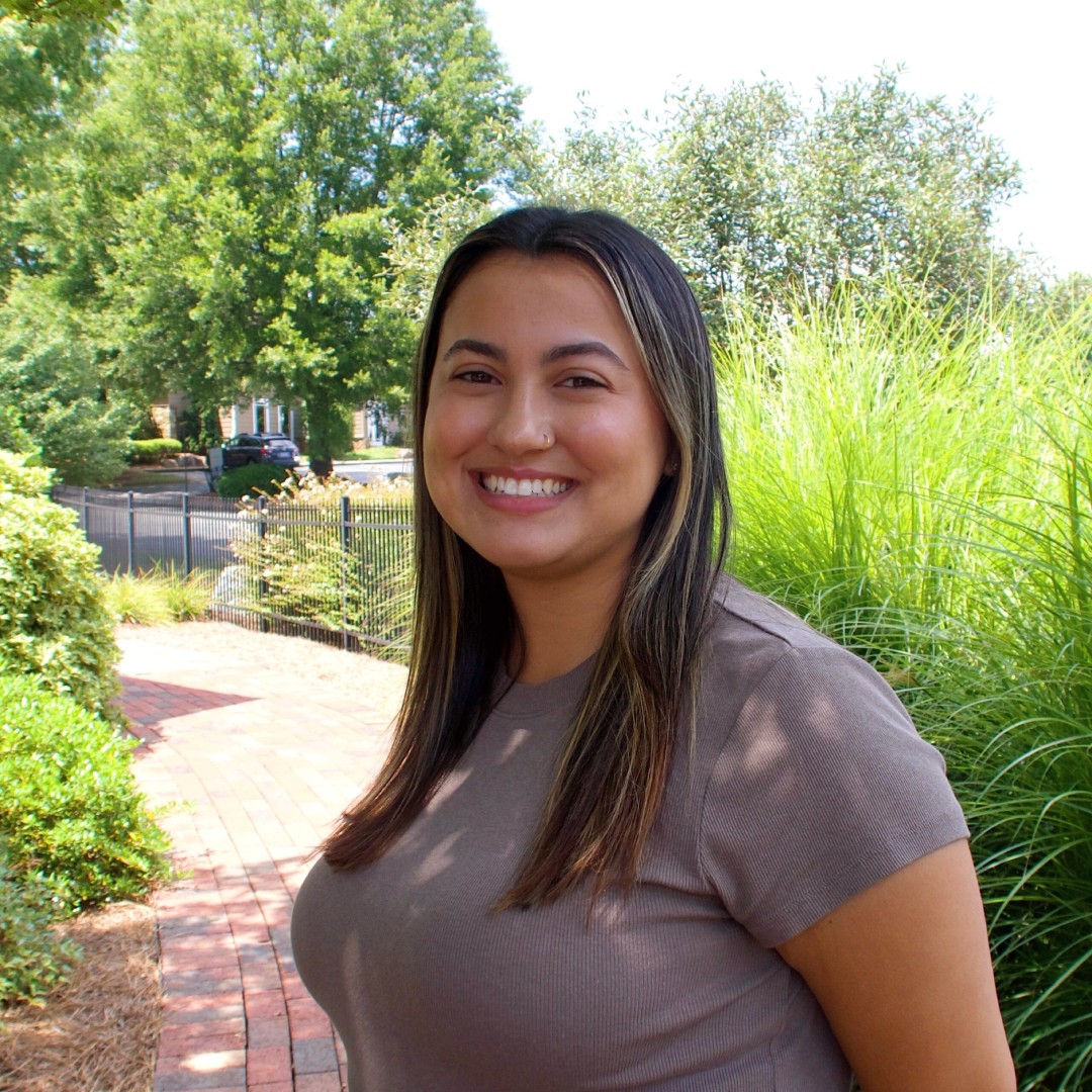 Smiling woman in a taupe shirt outdoors.